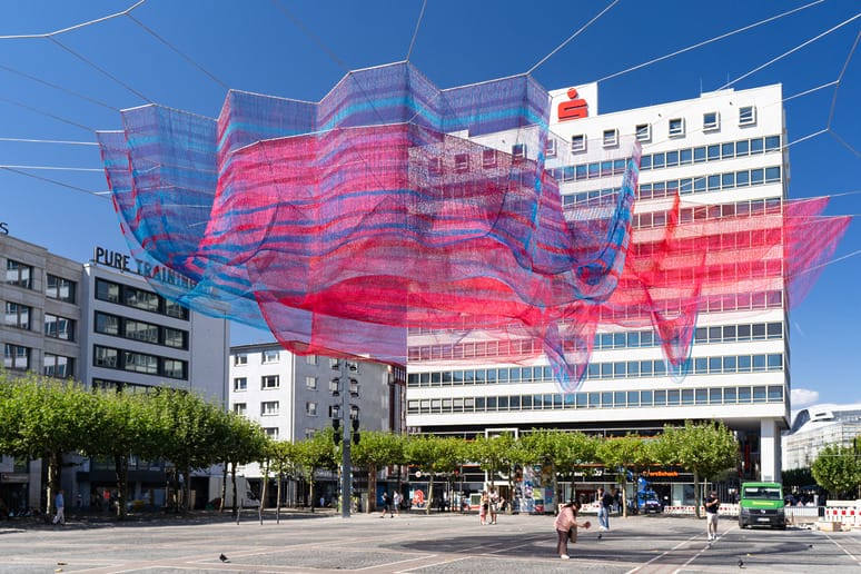 Janet Echelman suspends 103 kilometers of fiber over a Frankfurt plaza, lit by 24 fixtures mounted on its own support pylons